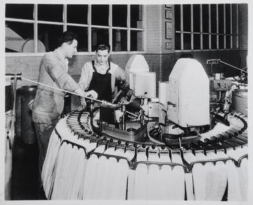 An overlooker explains to an apprentice the working of a noble comb used for wool-combing in the processes of worsted manufacture. Image used for one of the photographic illustrations in 